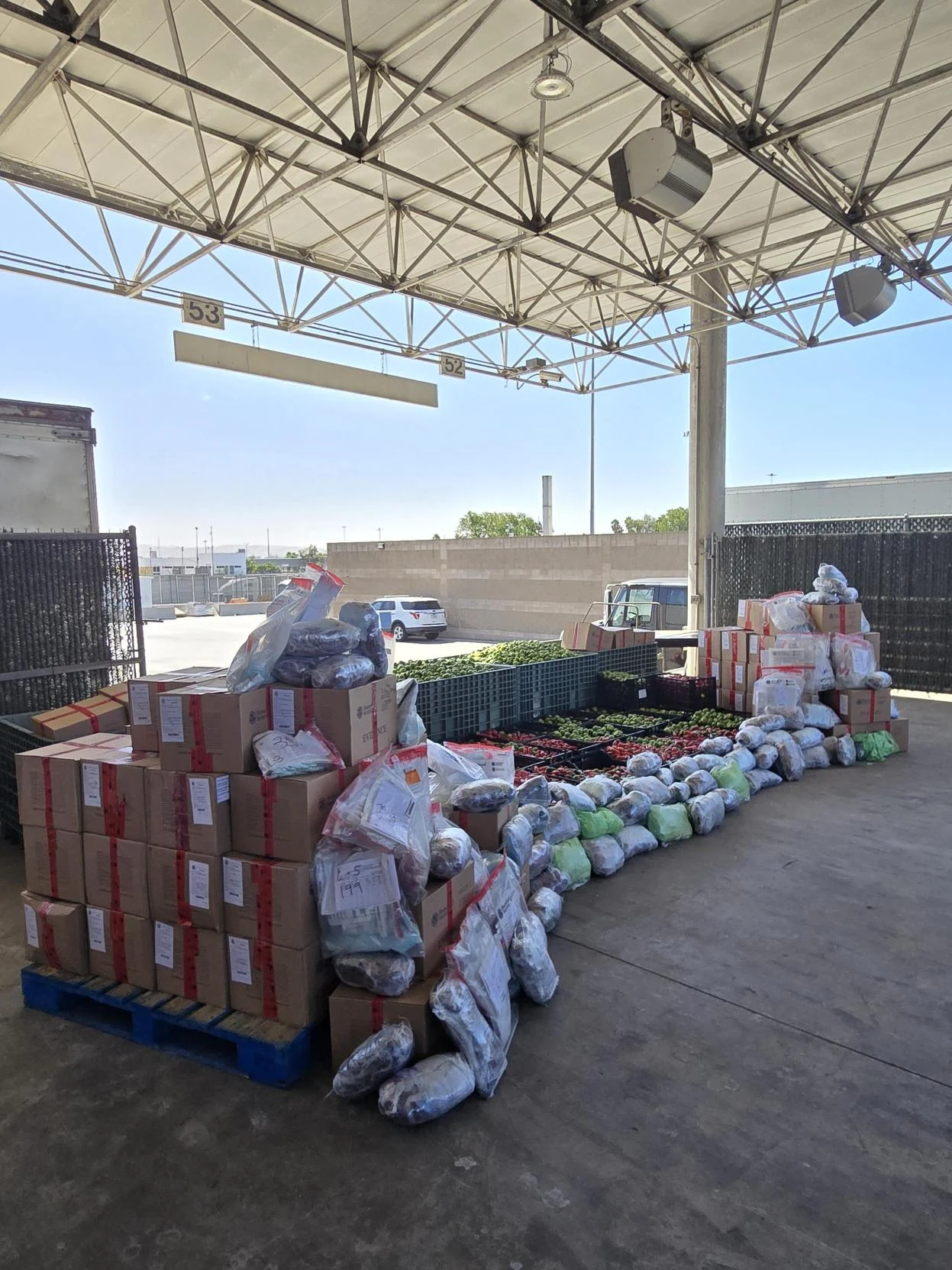 Bundles of methamphetamine in plastic wrap and stacked boxes on pallets beside crates of tomatillos at a covered inspection dock.