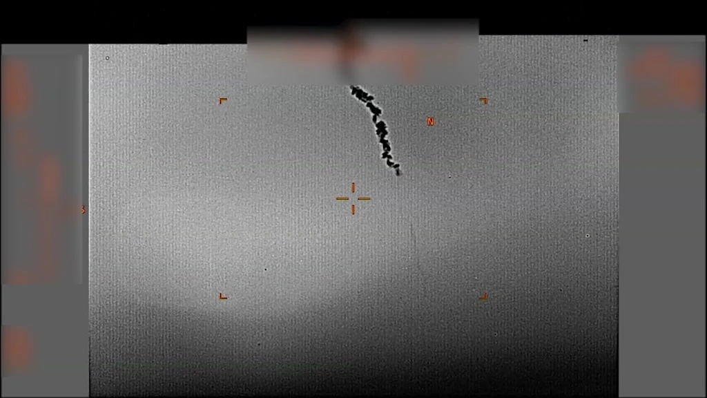 Grey infrared sensor view with an orange crosshair and corner brackets: a dark, jagged smoke trail falls diagonally from the top of the frame, with the side data panels blurred.