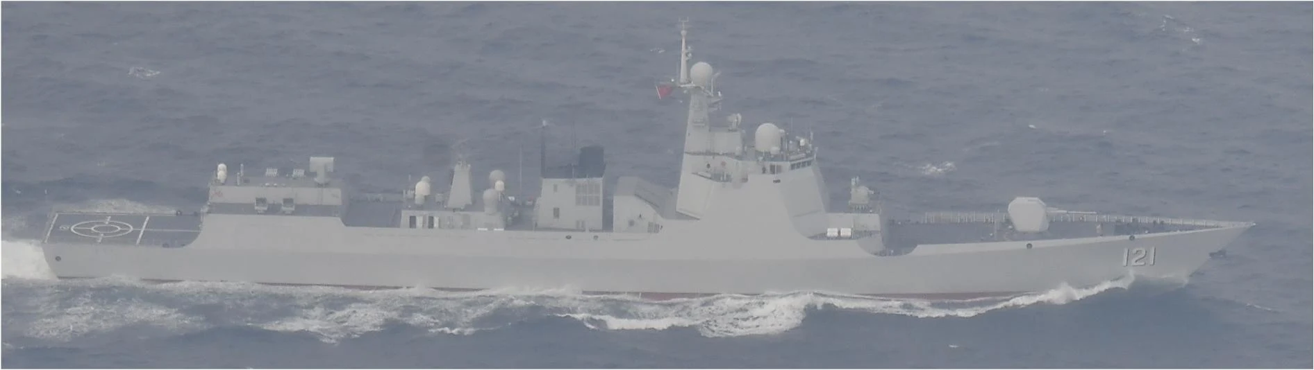 Grey Chinese navy destroyer in side view on choppy grey-blue sea, with hull number 121 on the bow, a helicopter deck at the stern, radar domes and a tall mast flying a red Chinese flag, and white wake along its side.