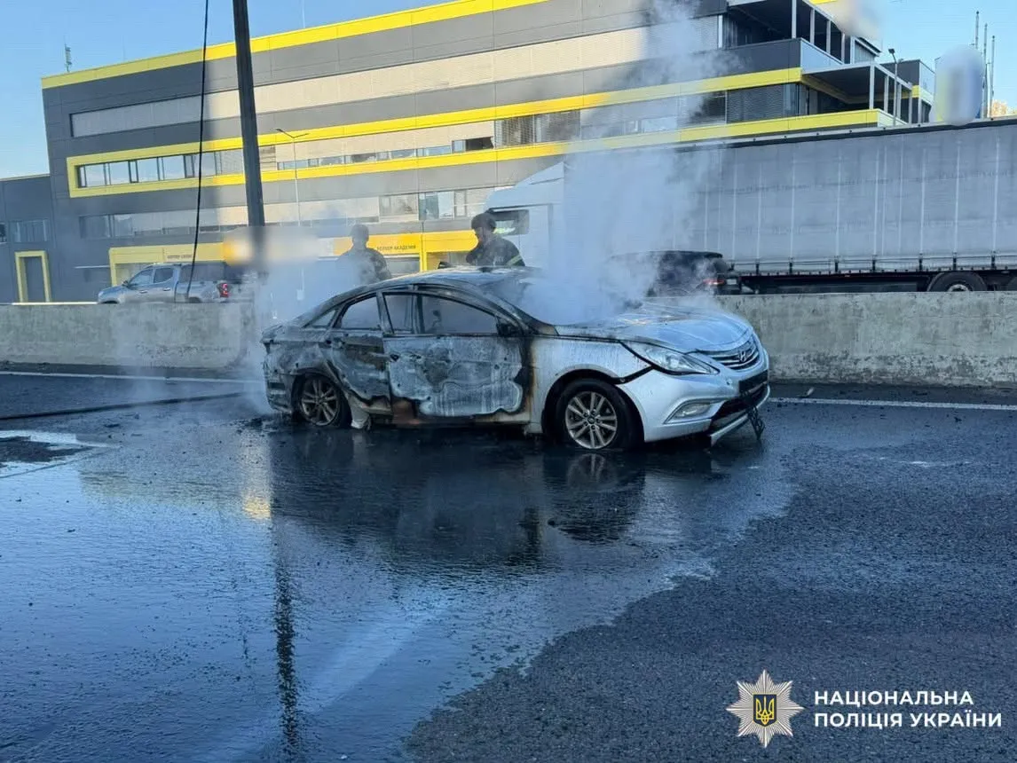 Photo released Oct 20, 2026 by the National Police of Ukraine: a burned-out car on the Kyiv-Odesa highway near Chabany after what Ukrainian officials say was a Russian drone strike that killed three people and injured four. Emergency workers stand in the background.