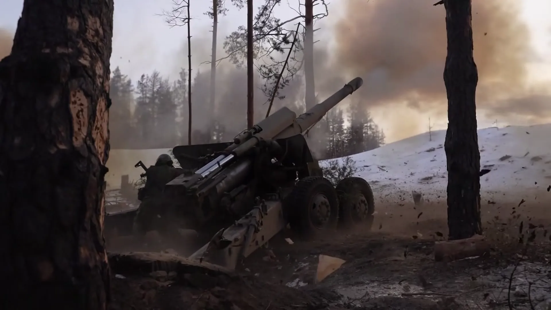 Frame at 30 s: towed howitzer firing among pine trees.